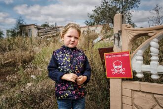 Veronika, 4, stands near a sign that reads "Danger of Mines". Chistovodivka, Kharkiv region, Ukraine (file, May 2025)